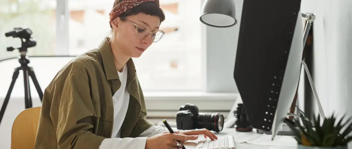 An image of a female photographer using a computer and external drive in a studio to edit images. 