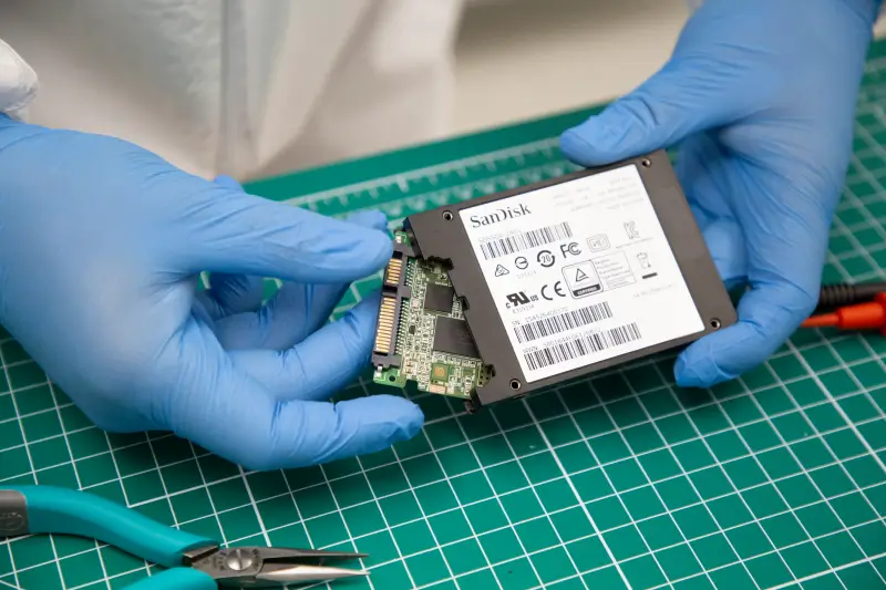 A photo of a data recovery engineer removing a circuit board from a SanDisk SSD.