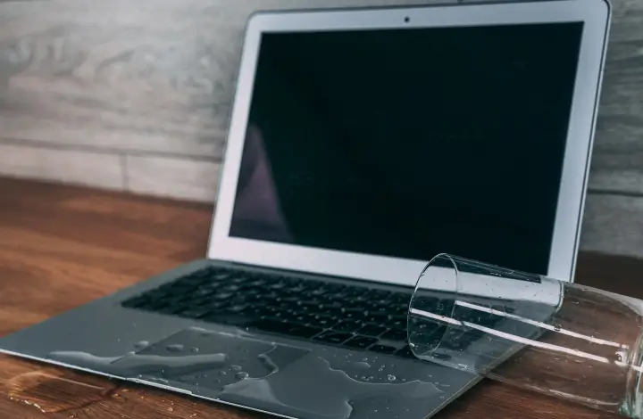 A glass of water spills on an open laptop, causing failure.
